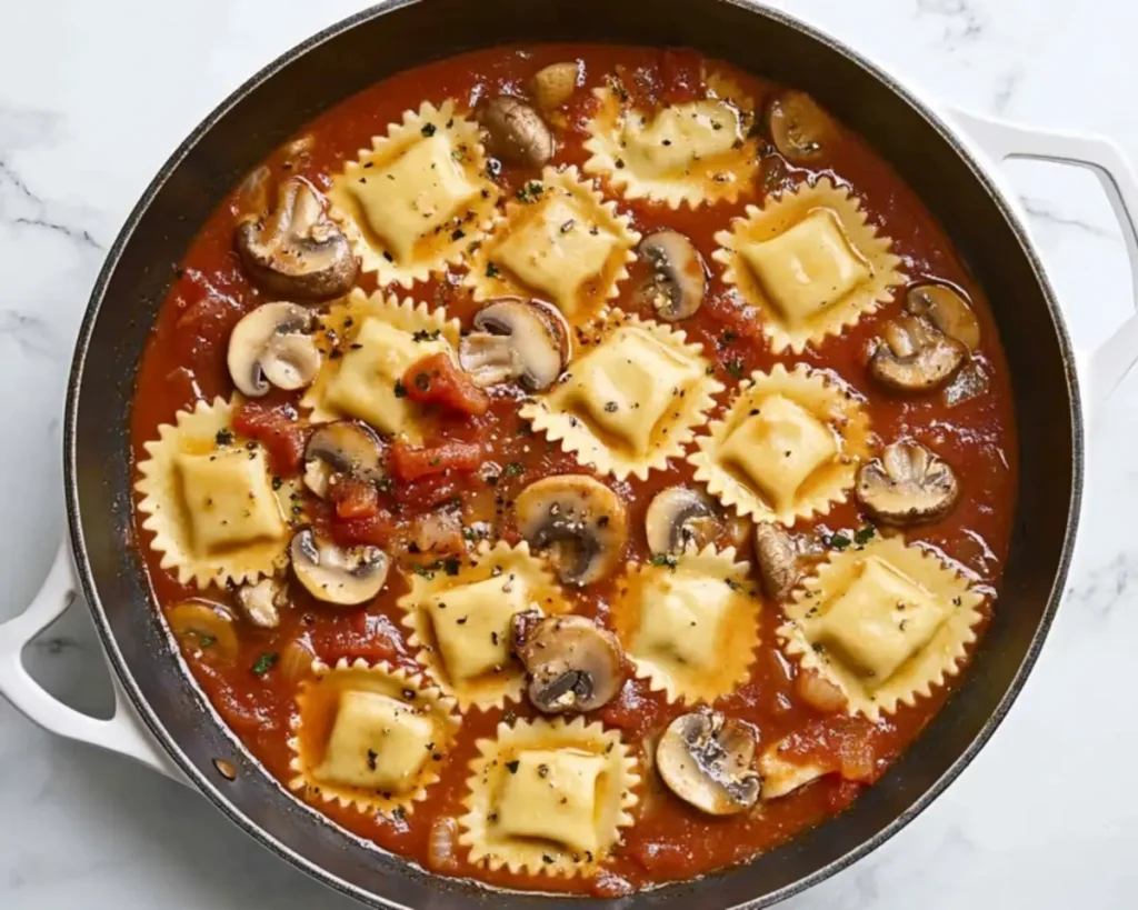 Cheese ravioli, sliced mushrooms, and tomato sauce in a skillet.