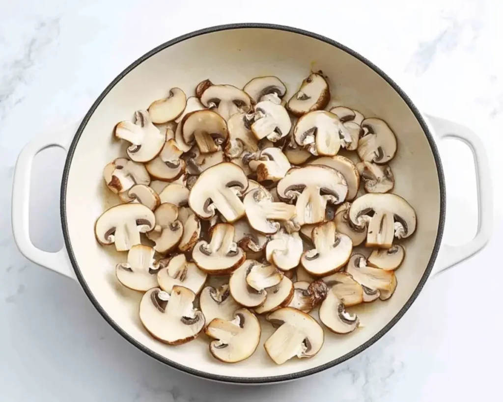 Sliced mushrooms sauteing in a deep skillet.