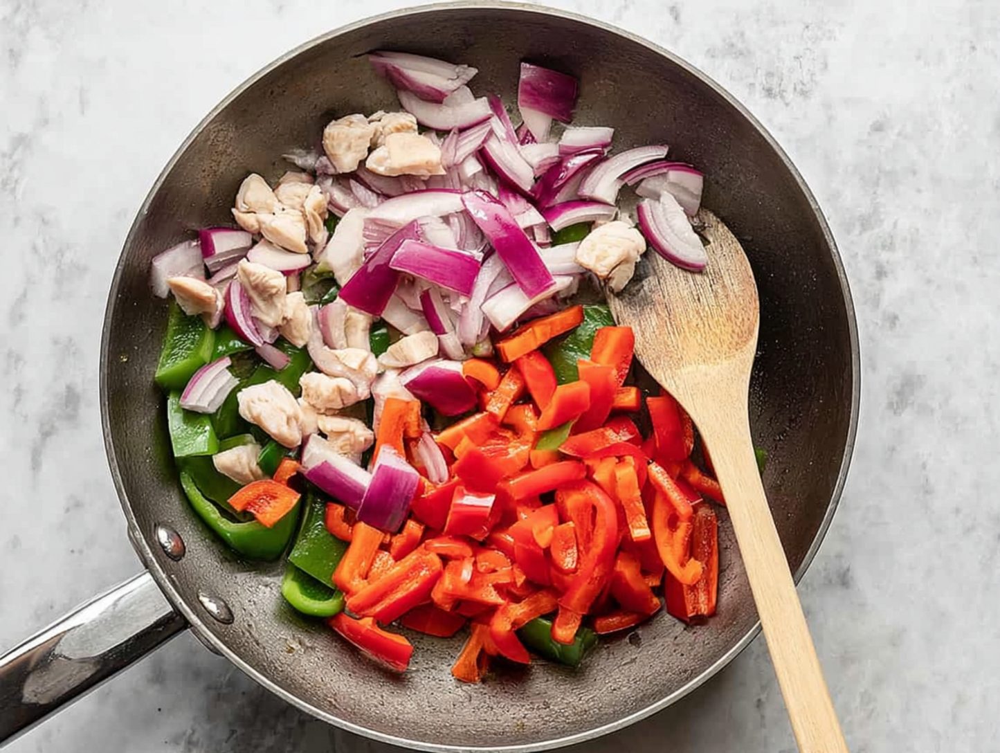 Skillet holding chicken with red pepper slices and onions