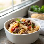Close-up of a bowl of High Protein Beef Pasta topped with fresh basil leaves.